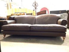 A Howard & Sons style sofa, upholstered in overstuffed brown leather, with squab cushions, raised on
