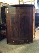 A 19thc mahogany bow front hanging corner cabinet with two panel doors enclosing a pair of shelves