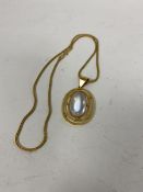 A moonstone cabouchon within a 9ct gold pendant, marked CM & Co. on a yellow metal chain (21cm) (5.