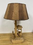 A hand carved table lamp in the form of a Man standing before a Well and Tree, base signed P.E,