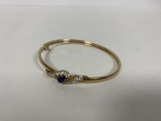 A 9ct gold bangle with central blue stone surrounded by clear paste stones (6cm) (7.84g)