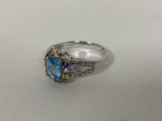 A 9ct gold ring set central cushion cut blue stone surrounded by multiple stones of varying hues (P)