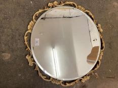 A circular wall mirror with bevelled edge within a parcel gilt scrolling leaf pierced frame, with