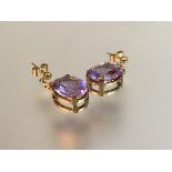 A pair of amethyst drop earrings, each with an oval-cut stone claw-set in yellow metal (believed