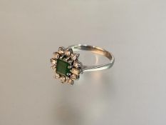 An emerald and diamond cluster ring, the central emerald within a band composed of a pair of