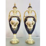 A pair of tall Coalport porcelain vases and covers, c. 1900, each painted to one side with a named