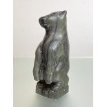 A North American Inuit green stone carving of a polar bear, modelled seated on it's haunches,