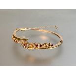 An 18ct gold bangle set with rubies and seed pearls, early 20th century, the oval band incorporating
