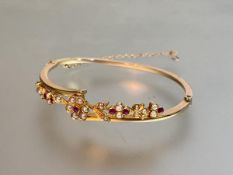 An 18ct gold bangle set with rubies and seed pearls, early 20th century, the oval band incorporating