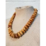 A single strand amber bead necklace, of graduated discs, with gilt-metal ball spacers, on a fish