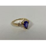 An 18ct gold ring with a pear shaped cut blue/purple stone, flanked by two half bands of diamonds (