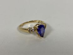 An 18ct gold ring with a pear shaped cut blue/purple stone, flanked by two half bands of diamonds (