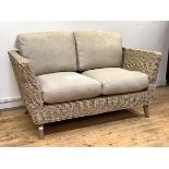 A wicker veranda two seat sofa, with oatmeal upholstered squab cushions, raised on turned