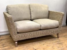 A wicker veranda two seat sofa, with oatmeal upholstered squab cushions, raised on turned