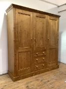 A Pine triple wardrobe, with centre hanging cupboard and three drawers, flanked by two cupboards, on