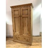 A traditional pine double wardrobe, two panelled doors enclosing hanging rail over drawer, raised on