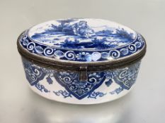 A French blue and white faience box, 19th century, oval, the domed cover painted with a courting