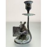 A patinated bronze novelty candlestick, modelled as a mouse reading a book, it's tail continuing