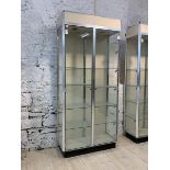 A modern glazed shop showcase, with two doors enclosing four shelves, on an ebonised base, H219cm,