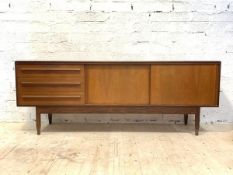 A mid century teak sideboard, the twin sliding doors enclosing a shelf, flanked by three drawers,