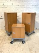 A pair of modern beech veneered cabinets, each with a door enclosing a shelf, raised on castors, (