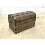 An early 20th century dome top steamer trunk, the hinged lid revealing plain interior, with carry