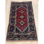 A hand knotted Caucasian rug, the red field with triple lozenge medallion and geometric design and