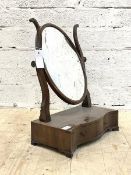 A Georgian mahogany toilet mirror, the oval mirror in conforming frame swivelling between scrolled