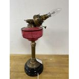 An early 20thc oil lamp with cranberry glass reservoir later converted to electricity, measures 50cm