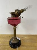 An early 20thc oil lamp with cranberry glass reservoir later converted to electricity, measures 50cm