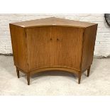 A Mid century teak floor standing corner cupboard, the twin concave doors enclosing shelves,