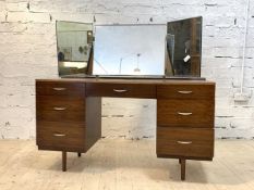 A mid century teak veneered dressing table, with triple swing mirror over one long and six short