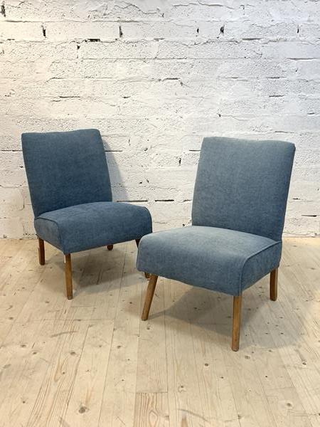 A pair of mid century lounge chairs, upholstered in blue fabric, raised on shaped tapering supports,