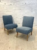 A pair of mid century lounge chairs, upholstered in blue fabric, raised on shaped tapering supports,