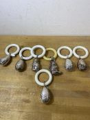 A collection of seven white metal baby rattles and teething rings, five in the shape of eggs with