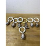 A collection of seven white metal baby rattles and teething rings, five in the shape of eggs with