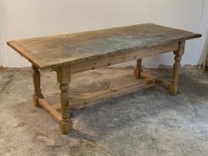 A pine farmhouse style dining table, the rectangular top on turned and block supports united by a