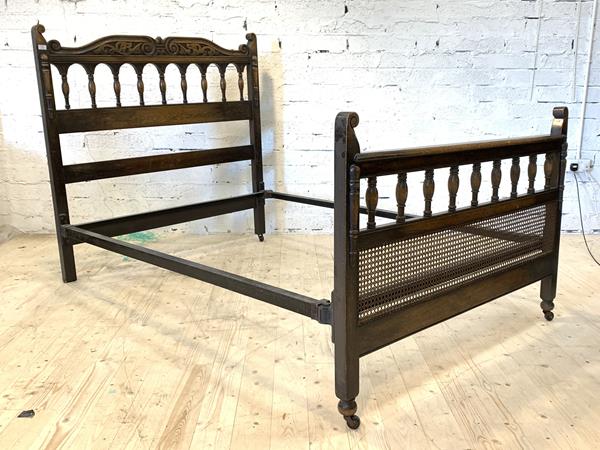 An oak 4'6" carved oak double bed, the footboard with cane panel, raised on castors, (One lacking)