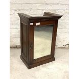 A Late 19th/early 20th century stained mahogany cupboard, the single glazed mirror door enclosing