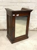 A Late 19th/early 20th century stained mahogany cupboard, the single glazed mirror door enclosing