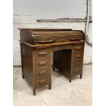 An early 20th century oak roll top desk, the tambour top revealing fitted interior, over two