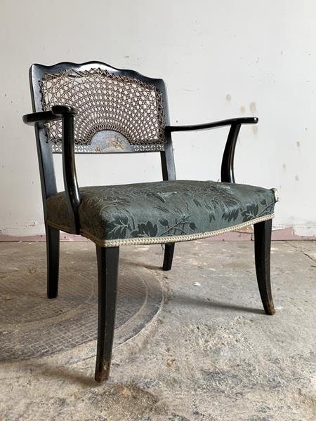 A circa 1930's ebonised bedroom chair, the cane back with gilt chinoiserie panel over open arms
