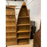 A modern floor standing pine bookshelf in the form of an upright row boat with four shelves,