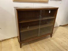 A Mid Century teak bookcase, the slightly bowed top over two sliding glass doors before two