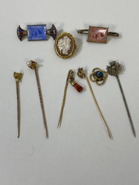 A collection of stick pins, one with carved coral pendant, some yellow metal, longest measures
