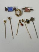 A collection of stick pins, one with carved coral pendant, some yellow metal, longest measures