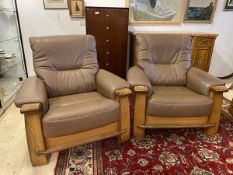 A pair of modern lounge armchairs with oak frames and chocolate brown leather back seat cushions and