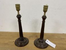 A pair of brass column style candlesticks, on carved wooden bases, measure 26cm high