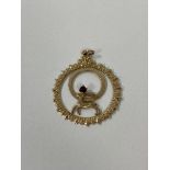 A 9ct London gold pendant of circular form with horned animal and single red stone, measures 3.5cm