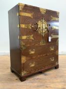 A Vietnamese brass bound stained hardwood cabinet on chest, the twin doors with brass strap hinges
